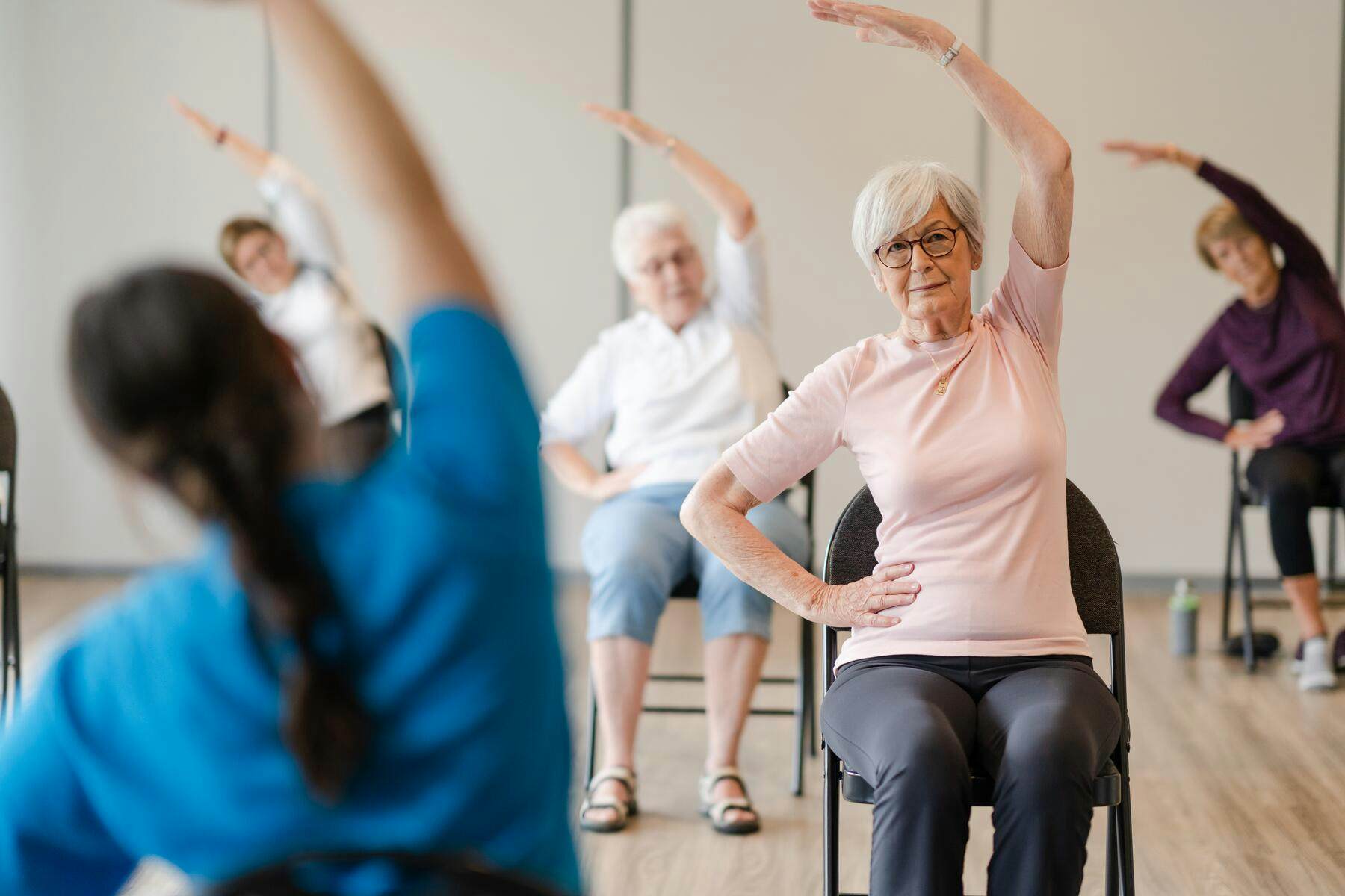 Senior residents performing chair yoga on chair with the instructor
