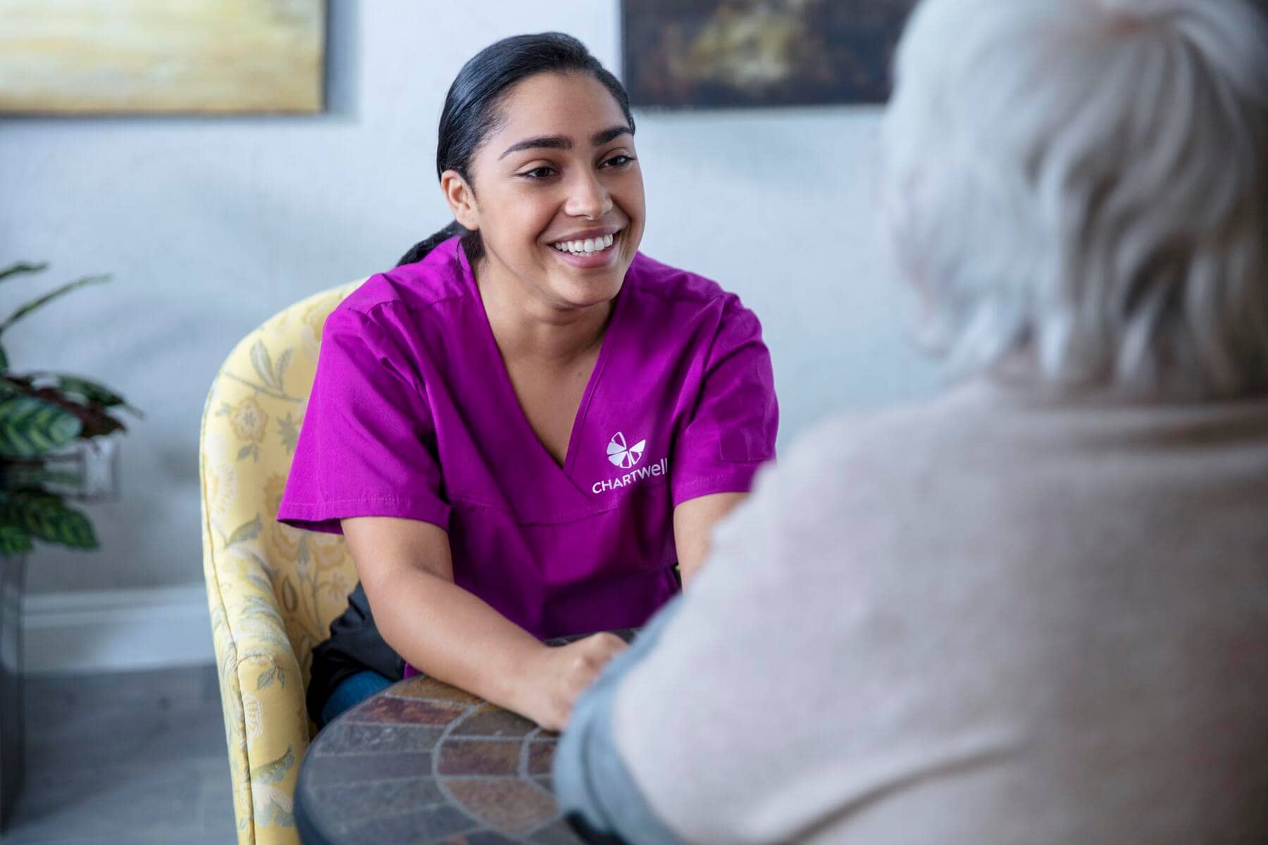 Chartwell care support staff sitting with the senior resident, holding hands smiling and having cheerful conversation.