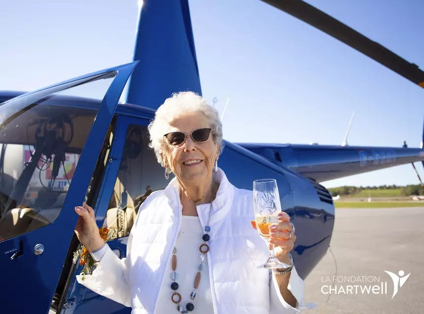 Femme âgée tenant une coupe de champagne devant l'hélicoptère