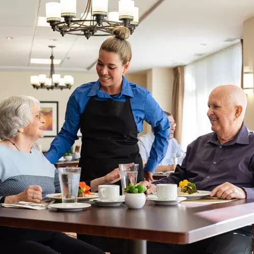 Chartwell Server having a pleasant conversation with the Senior couple at the dinning table / Le serveur de Chartwell a une conversation agréable avec le couple de personnes âgées à la table à manger