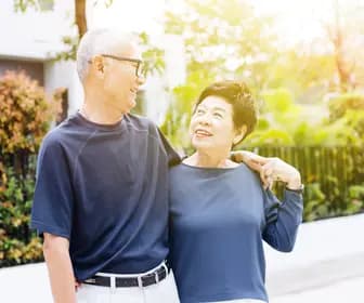 Happy retired senior Asian couple walking and looking at each other with romance in outdoor park and house in background