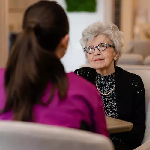 Senior woman sitting down talking with Chartwell staff member. Femme âgée assise discutant avec un membre du personnel de Chartwell.