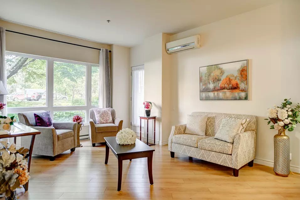 Salon avec divan sofa et air climatisé et grande fenêtre dans appartement modèle Chartwell Appartements de Bordeaux résidence pour retraités