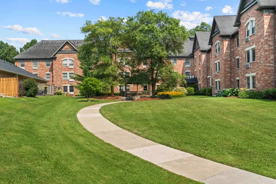 Landscaped courtyard with pathway and brick exterior building at Chartwell Riverside apartment / Cour paysagée avec sentier et immeuble en briques à Chartwell Riverside appartement