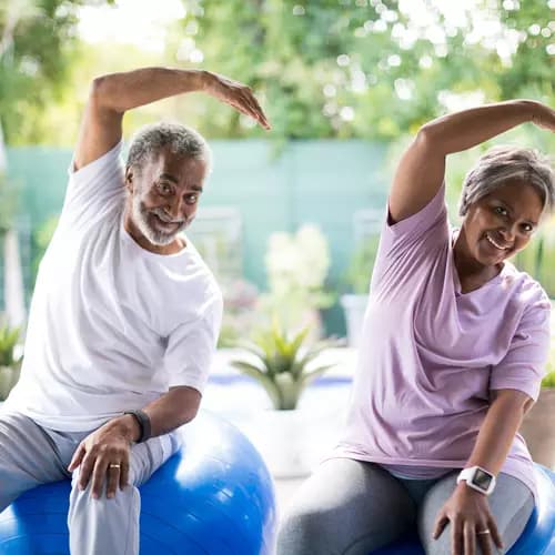 Senior couple is doing a stretch while sitting on a gym ball / Un couple de seniors fait des étirements en s'asseyant sur un ballon de gymnastique