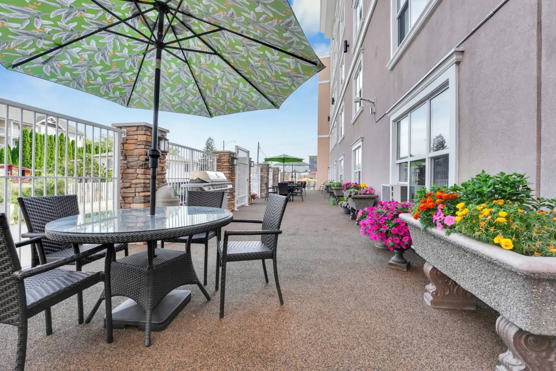 Exterior patio at Chartwell Kamloop with parasol table, chairs and flower beds / Terrasse extérieure de Chartwell Kamloop avec table parasol, chaises et parterres de fleurs