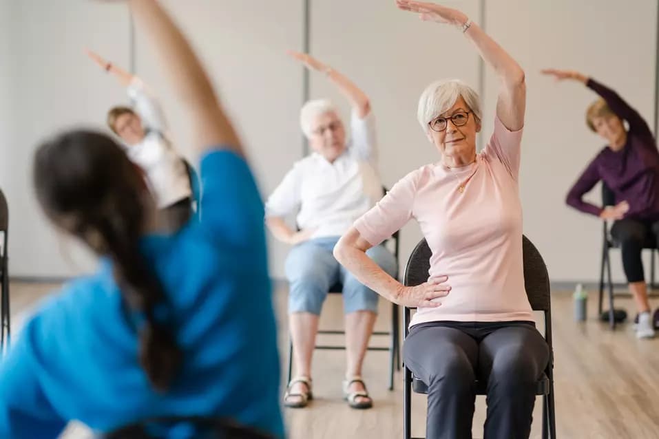 Senior residents performing chair yoga on chair with the instructor / Résidents seniors pratiquant le yoga sur chaise avec leur instructeur