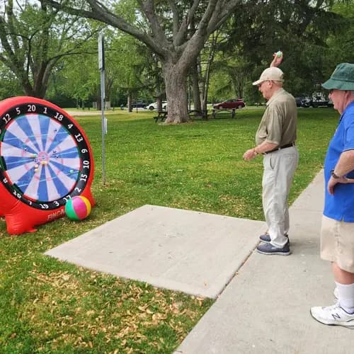 Residents playing a large inflatable dart game outdoors / Résidents jouant à un grand jeu de fléchettes gonflable à l’extérieur