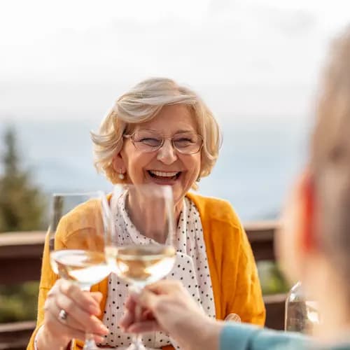 Brightly smiling senior woman tossing a wine glass with her partner / Une femme âgée au sourire radieux partageant un verre de vin avec son partenaire