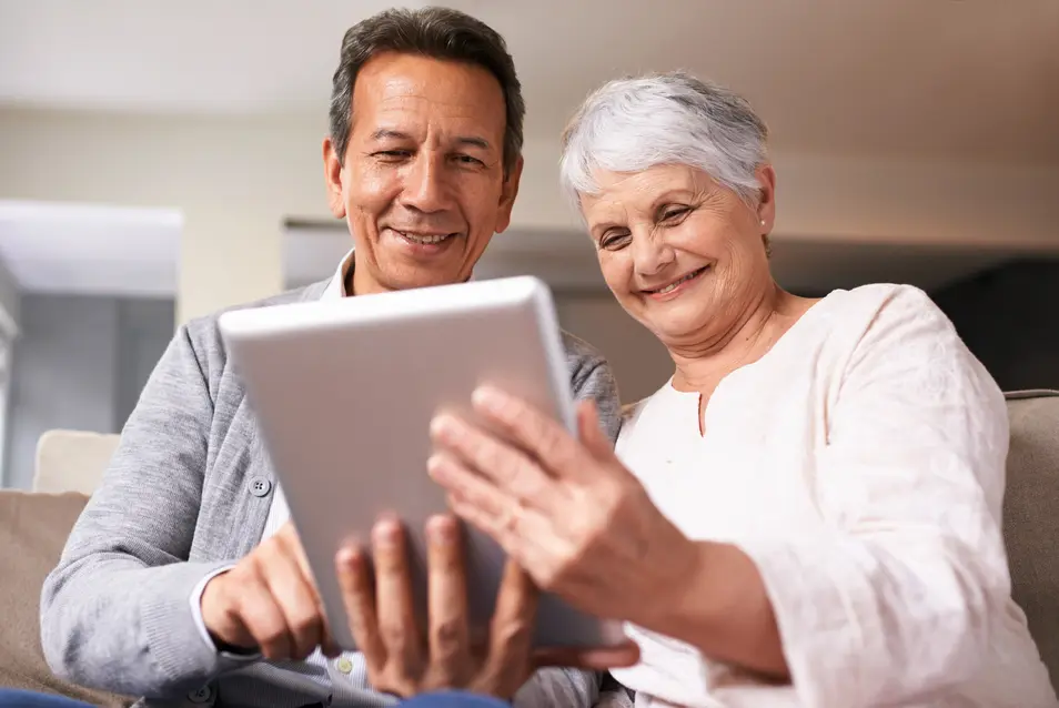 Older adult and adult family member looking at a tablet together at home. / Personne âgée et proche adulte regardant une tablette ensemble à la maison.