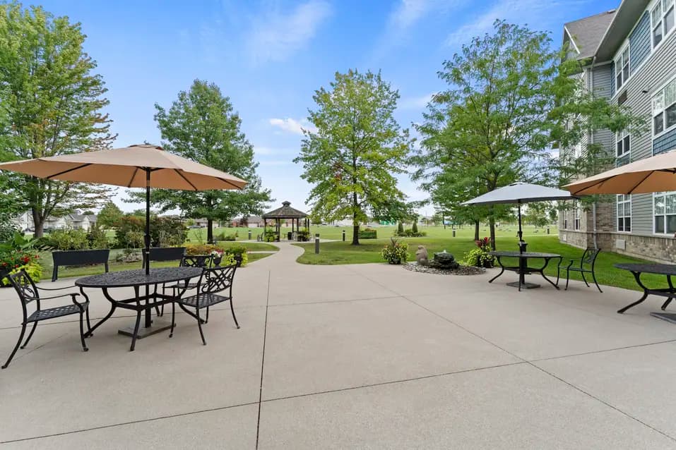 Outdoor patio with tables, umbrellas, and landscaped grounds at Chartwell Royal Oak Village. / Terrasse extérieure avec tables, parasols et aménagement paysager au Chartwell Royal Oak Village.