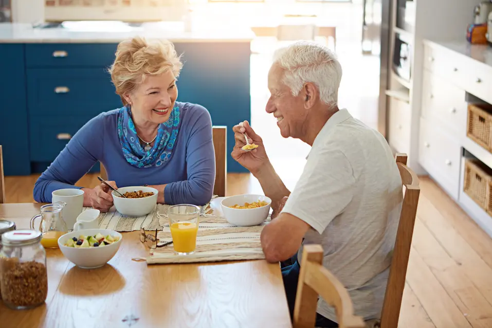 Old couple, smile and eating at dining table with breakfast, healthy food or talk for bonding together. Married, elderly people and happy in home with morning meal, nutrition and love for retirement