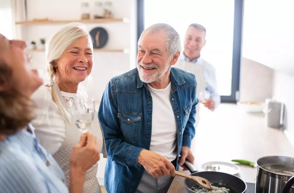 A group of seniors are enjoying cooking together while having a glass of champaign / Un groupe de personnes âgées prend plaisir à cuisiner ensemble tout en buvant un verre de champagne