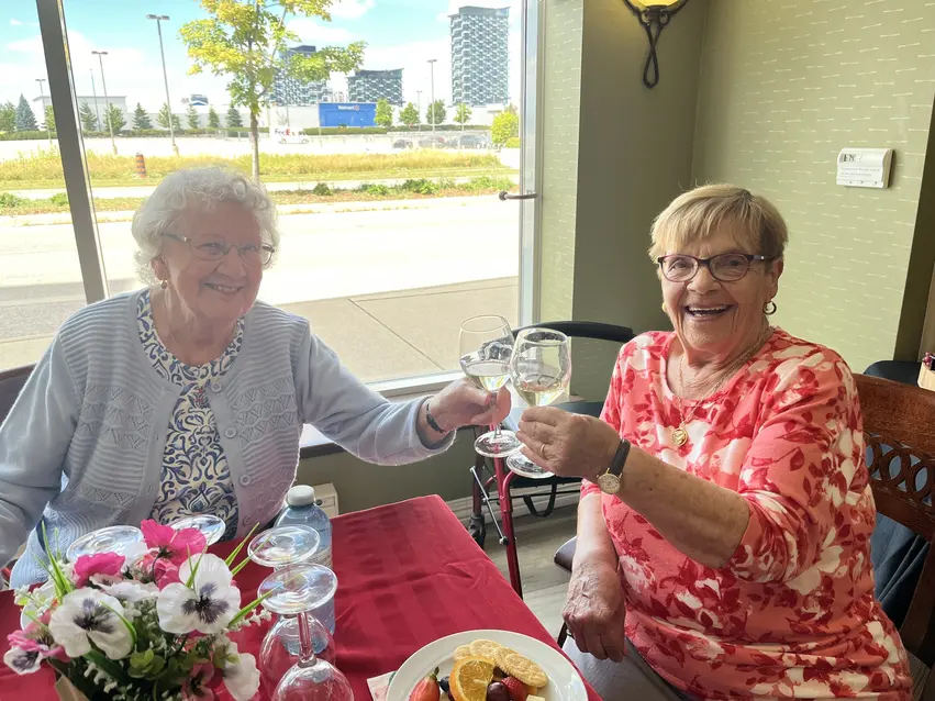 Residents toasting with wine glasses during a meal / Résidentes trinquant avec des verres de vin pendant un repas