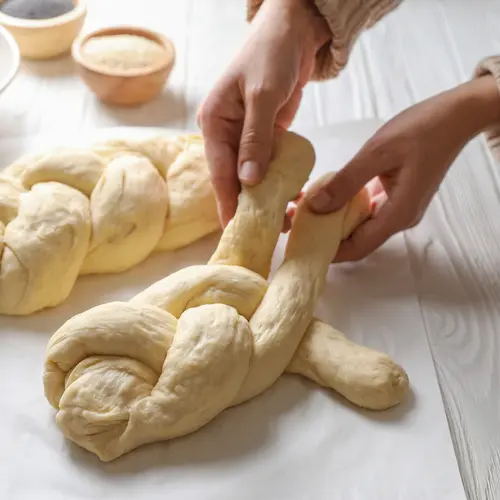 Woman cooking braided bread at white wooden table in kitchen, closeup. Traditional Shabbat challah