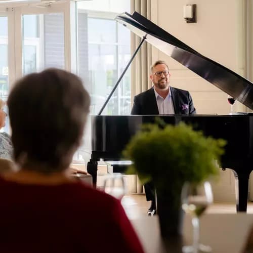 Seniors gathered and listening to a man playing a grand piano / Des personnes âgées se rassemblent et écoutent un homme jouant du piano à queue