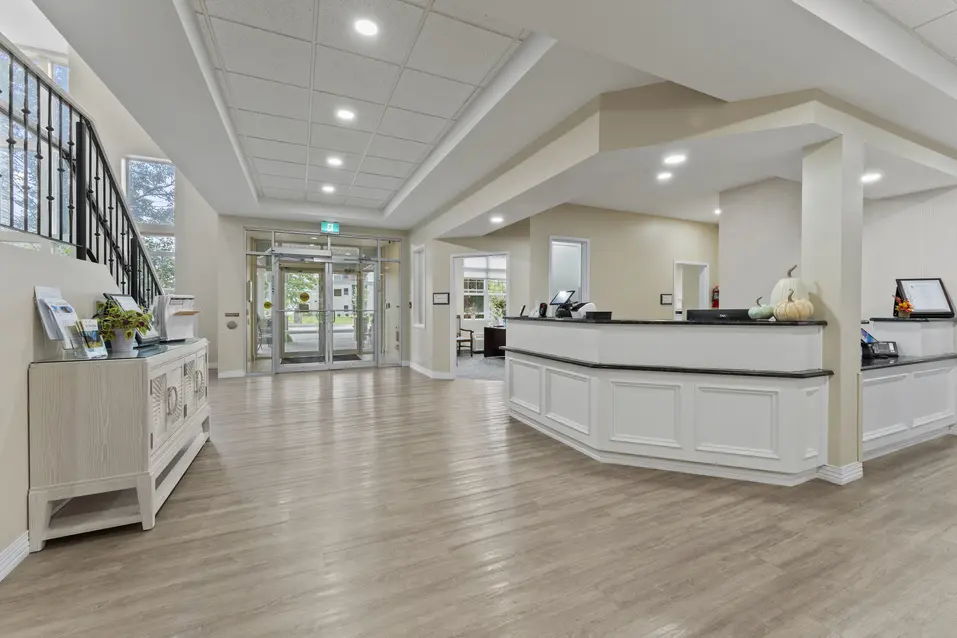 Bright entrance lobby with reception desk, seating areas, and high ceilings at Chartwell Royal Oak Village. / Hall d’entrée lumineux avec réception, espaces de détente et plafonds élevés au Chartwell Royal Oak Village.