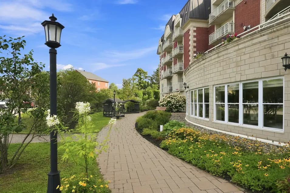Sentier pavé bordé de jardins paysagers le long de la résidence au Chartwell Seigneuries du Carrefour. / Paved pathway lined with landscaped gardens alongside the residence at Chartwell Seigneuries du Carrefour.