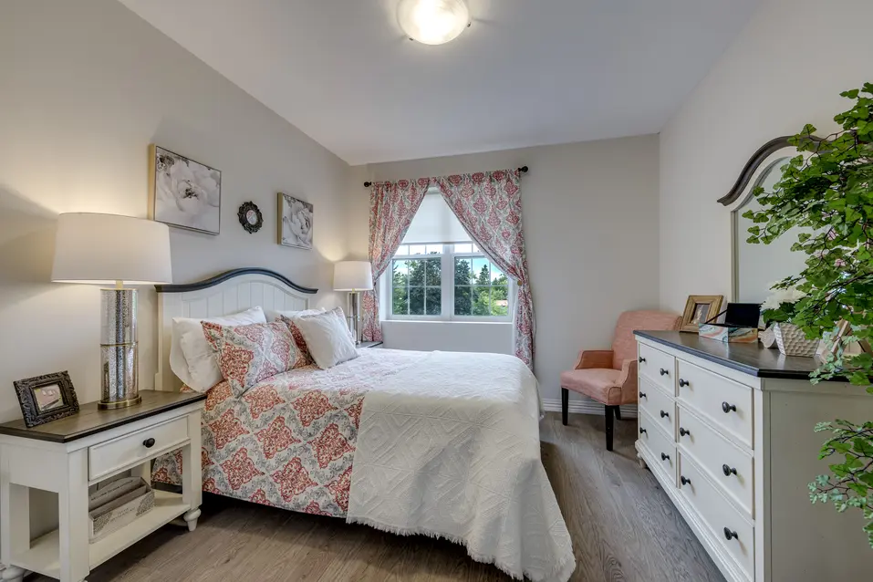 Model suite bedroom with large window and comfortable seating at Chartwell Welland / Chambre de la suite témoin avec grande fenêtre et fauteuil confortable à Chartwell Welland