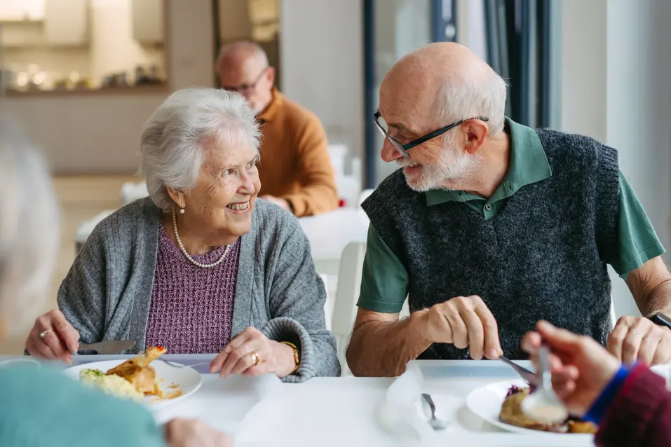 Old couple people having lunch with supportive caregiver in community center cafeteria.