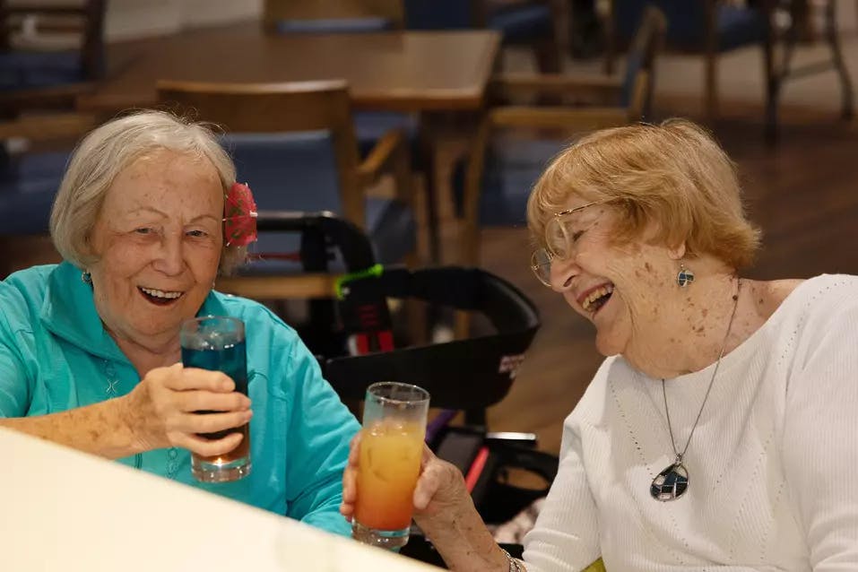 Two senior ladies smiling and having drinks together.  Deux femmes âgées souriant et prenant un verre ensemble. 