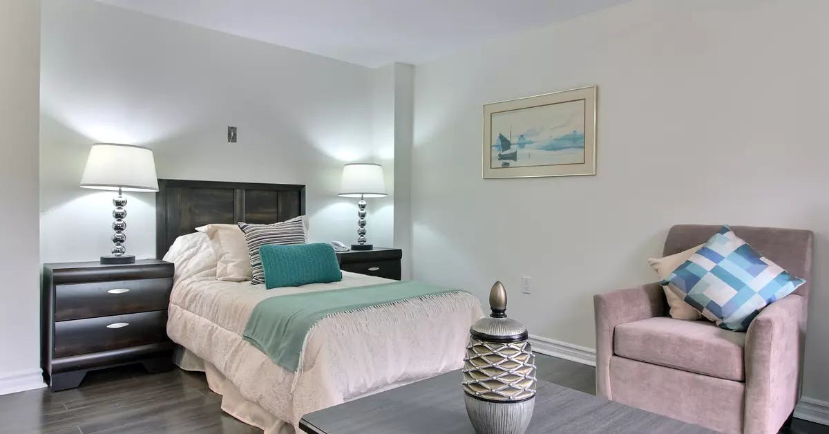 Chambre à coucher avec lit double et fauteuil dans appartement modèle Chartwell Domaine de Bordeaux résidence pour retraités