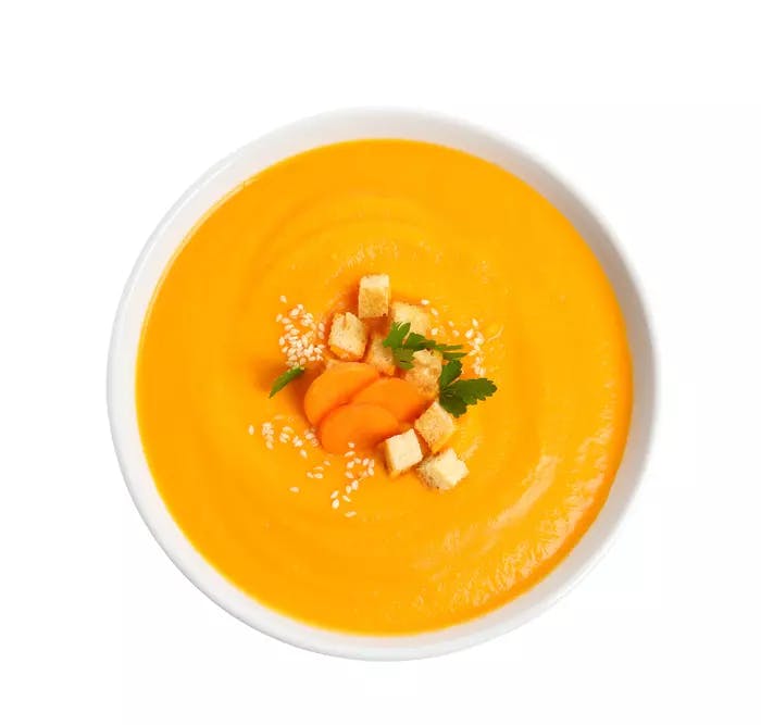 Carrot soup in a bowl with carrot, crouton and basil garnish