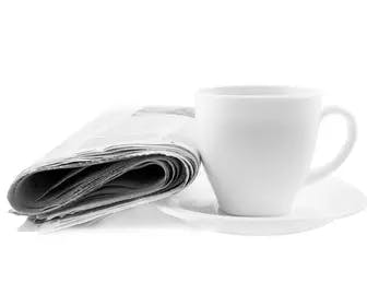 a newspaper leaning against a cup of coffee