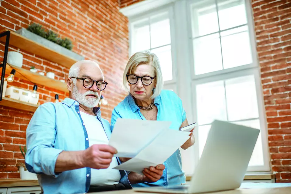 Senior couple is evaluating documents in front of their laptop / Un couple de seniors évalue des documents devant leur ordinateur portable