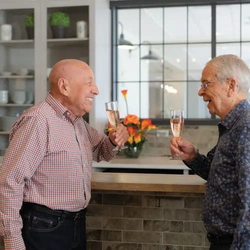 Senior men are having a joyful conversation while holding a champaign glasses in their hands / Des hommes âgés discutent joyeusement en tenant un verre de champagne à la main.
