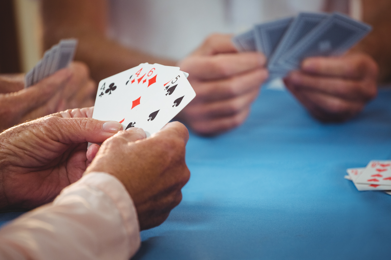 Close up of people's hands at a table holding playing cards. Gros plan sur les mains de personnes attablées avec des cartes à jouer.