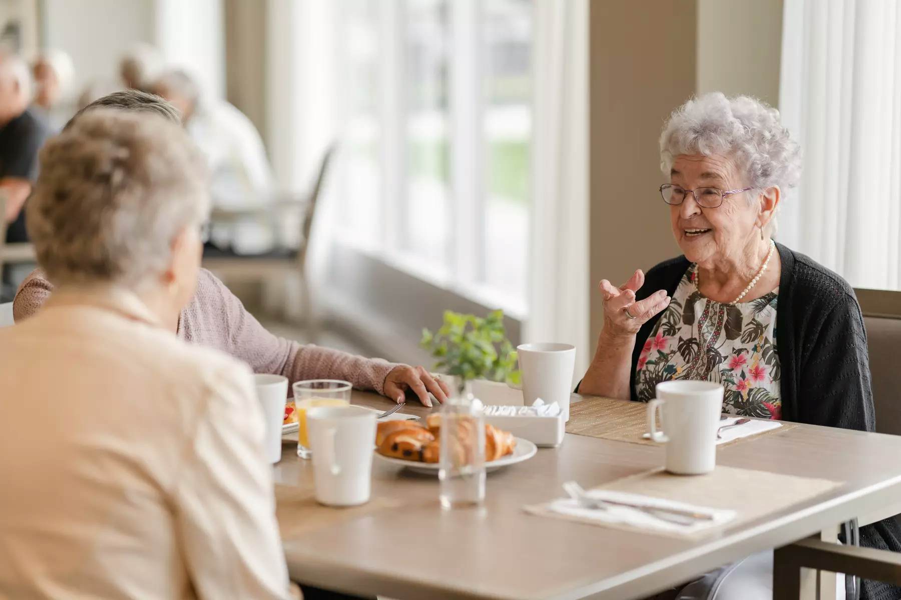 Senior residents having a pleasant conversation at the dinning table while enjoying a cup of coffee