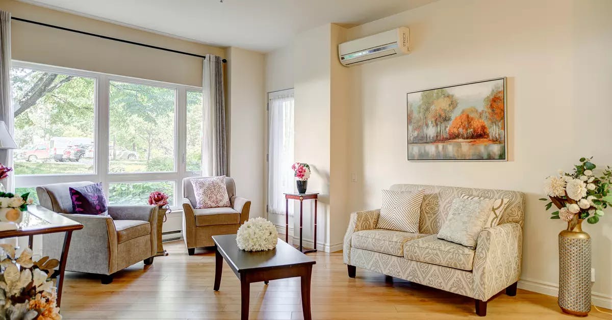Salon avec divan sofa et air climatisé et grande fenêtre dans appartement modèle Chartwell Appartements de Bordeaux résidence pour retraités
