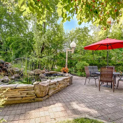 Salon extérieur au bord d'un étang avec table parasol chez Chartwell Manoir Kirkland / Outdoor sitting area beside a pond with a parasol table at Chartwell Manoir Kirkland
